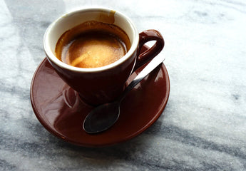 Espressomachine, waar de vers gezette espresso in het kopje loopt. Naast de machine een schaaltje met brownies en een Zeeuwse Bolus. Ter decoratie een paar koffiebonen. Ver gebrande espressobonen koop je bij de Zeeuwse Sommelier.